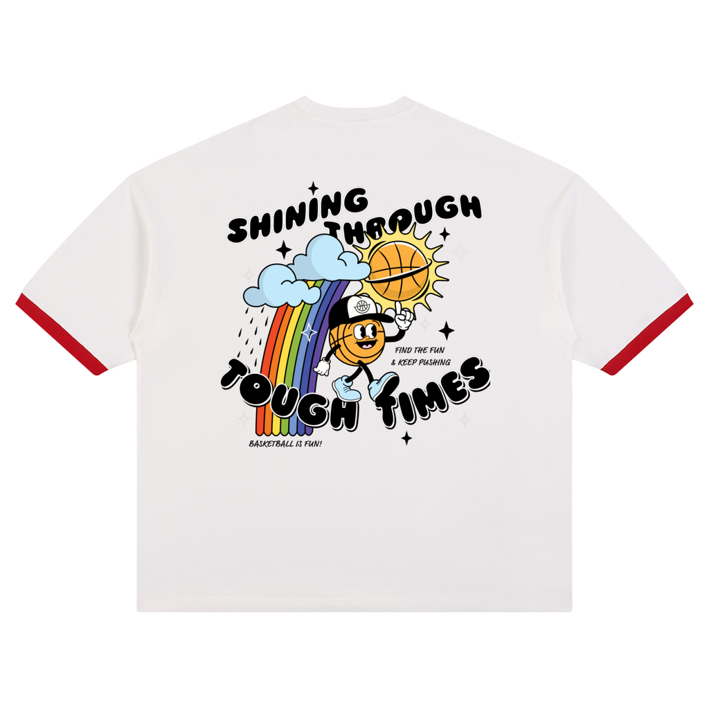 White ringer t-shirt with red trim on the sleeves and a colorful graphic on the back featuring a cartoon basketball, rainbow, and the text 'SHINING THROUGH TOUGH TIMES'.