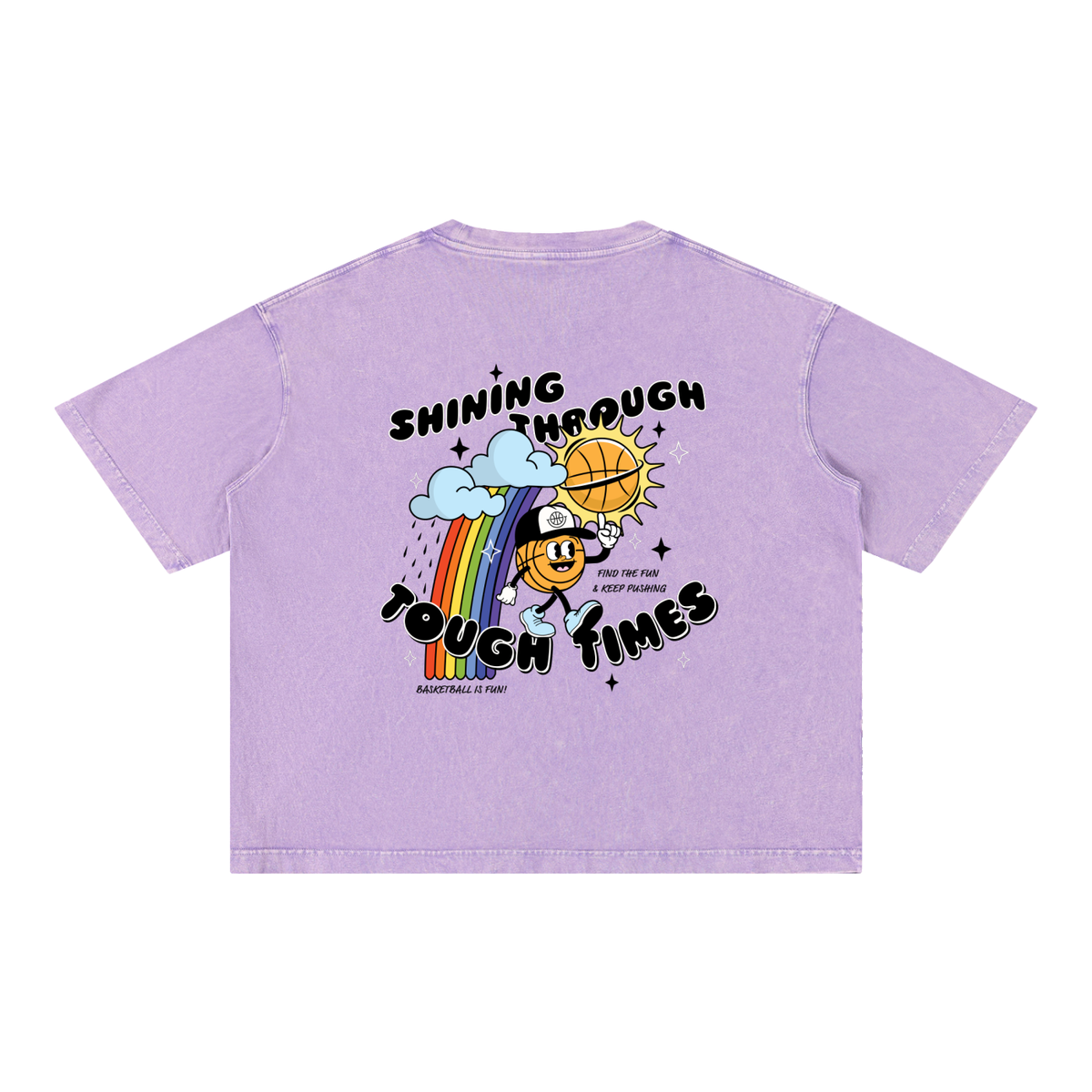 A light purple short-sleeve t-shirt shown from the back, featuring a colorful graphic print with a cartoon basketball character, a rainbow, clouds, and the text 'SHINING THROUGH TOUGH TIMES' and 'BASKETBALL IS FUN'.
